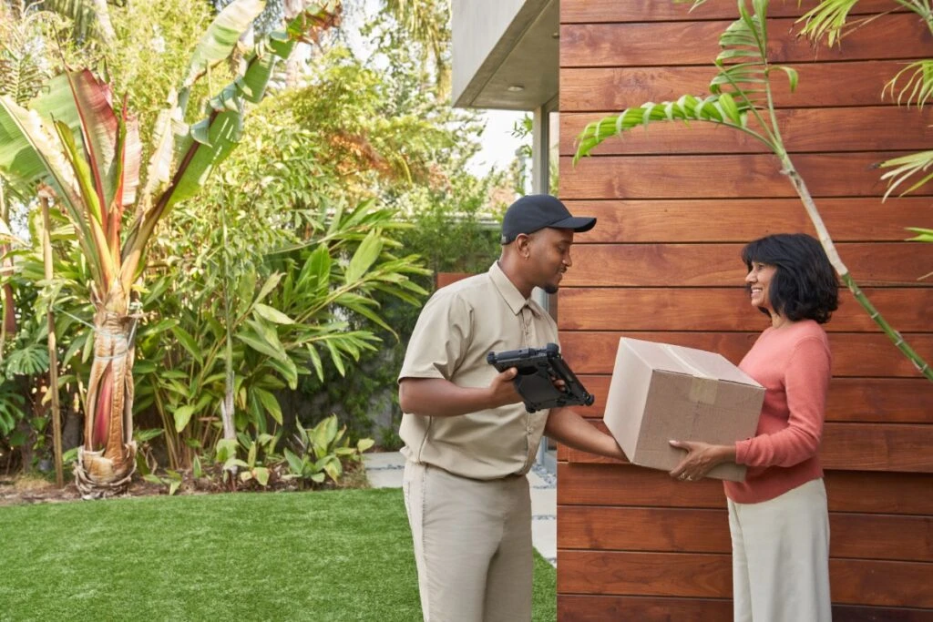 Delivery person handing a package to a satisfied customer at the customer’s doorstep. Keywords: Dynamics 365; purchase; online ordering; ecommerce; delivering a box; Surface tablet; at home; receiving an order; driver; man; woman