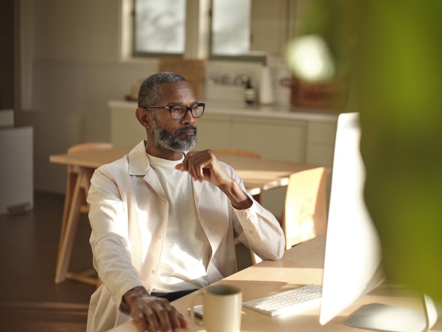 Man sitting at wooden table looking at the the screen on a desktop computer.