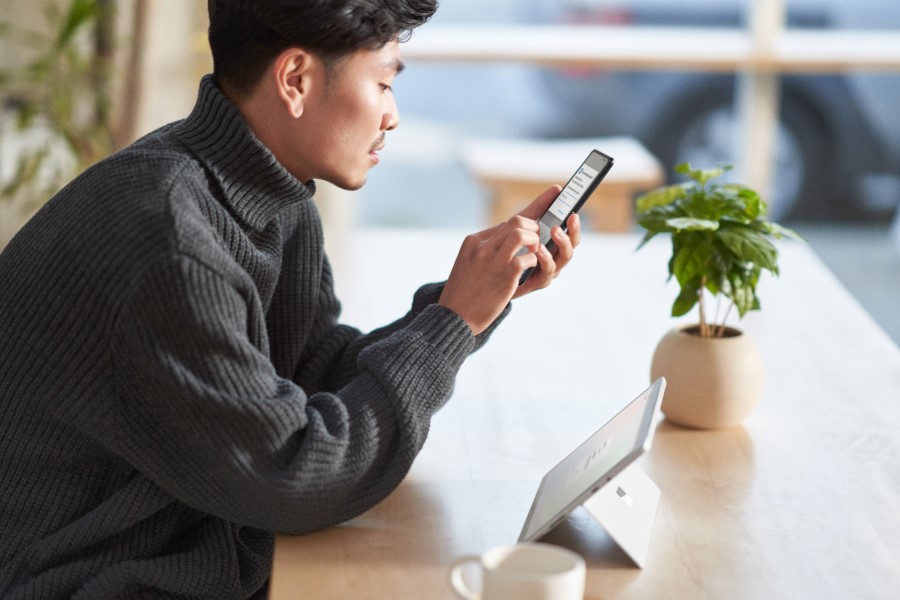 Man sitting at a table, looking at a mobile phone in his hand.