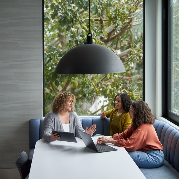 Three people sitting at a table talking with a tablet and a laptop